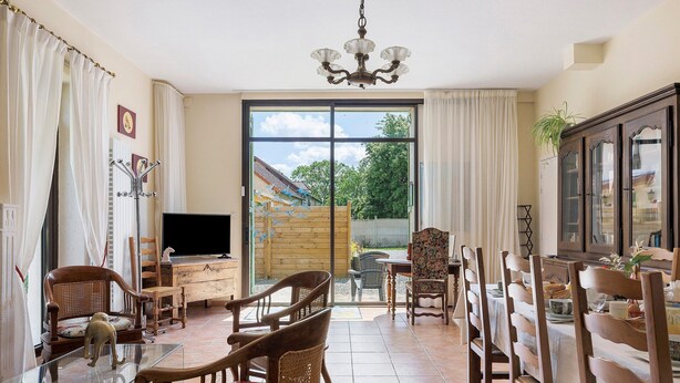 Comedor con sillas de madera, una mesa de vidrio, un televisor y vistas al exterior a través de un gran ventanal corredero.