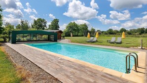 A swimming pool with a wooden deck, lounge chairs, and a covered seating area. - Bed and Breakfast 'Les Malvaux - Chambre Verte' with Shared Pool, Shared Terrace and Wi-Fi (Huriel)