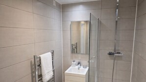 Moderni kylpyhuone, jossa on lasinen suihkuseinä, valkoinen pesuallas ja pyyhekoukku.