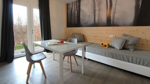 Quarto moderno com mesa de vidro, duas cadeiras, um sofá e um mural grande com tema de floresta.