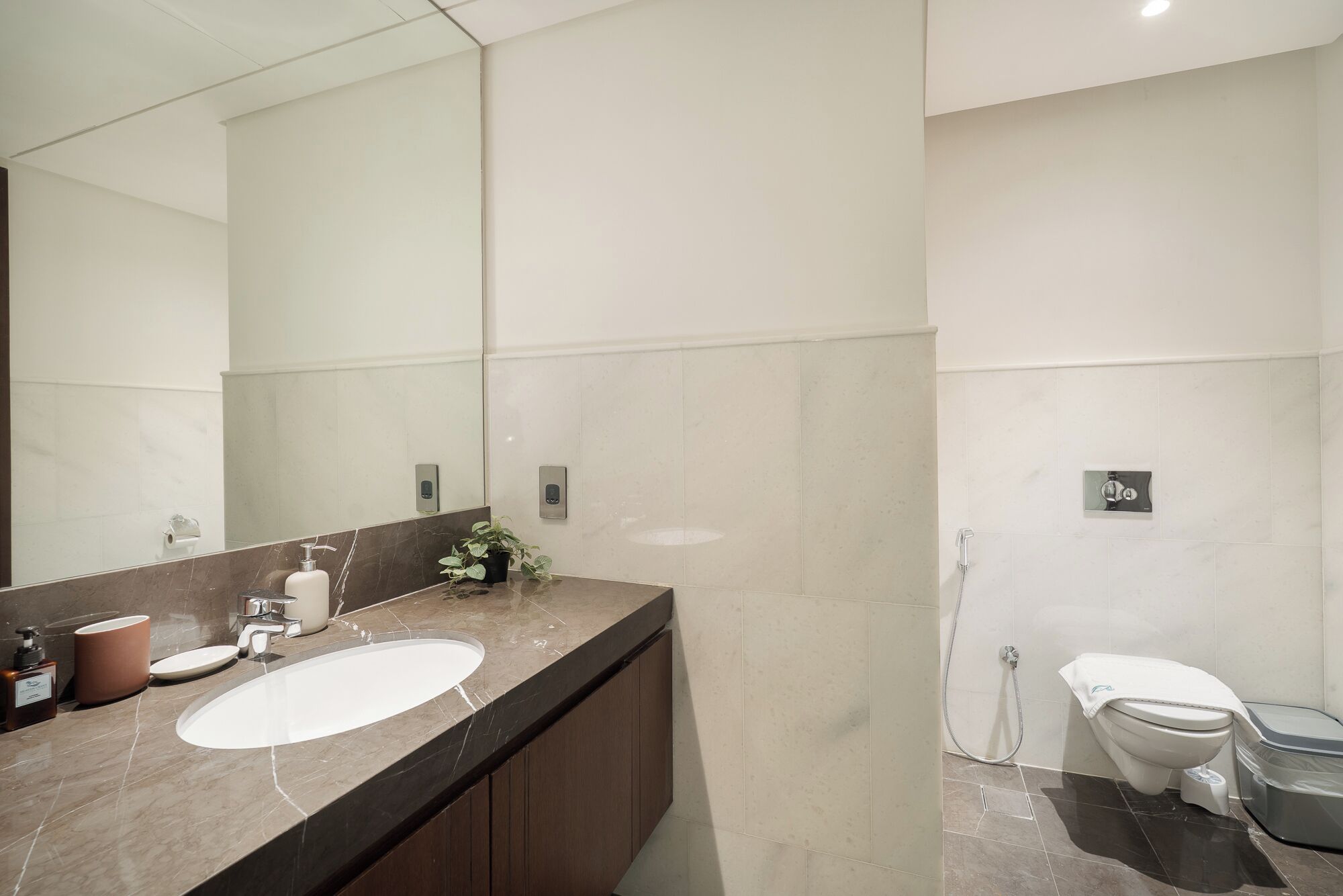 A modern bathroom with a large mirror, two sinks, a toilet, and a shower.