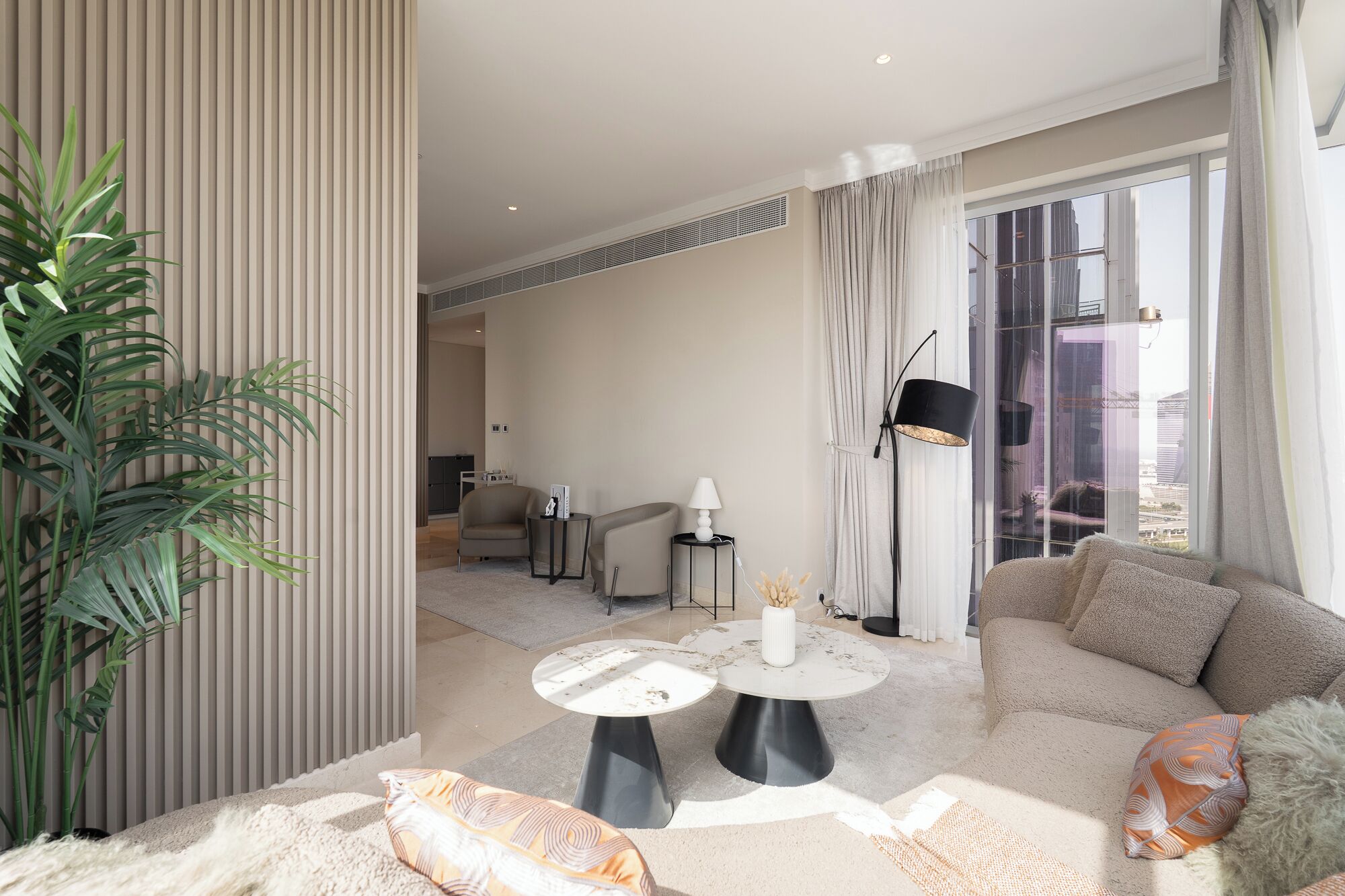 A modern living room with a sofa, two round tables, a lamp, and a large window with curtains.