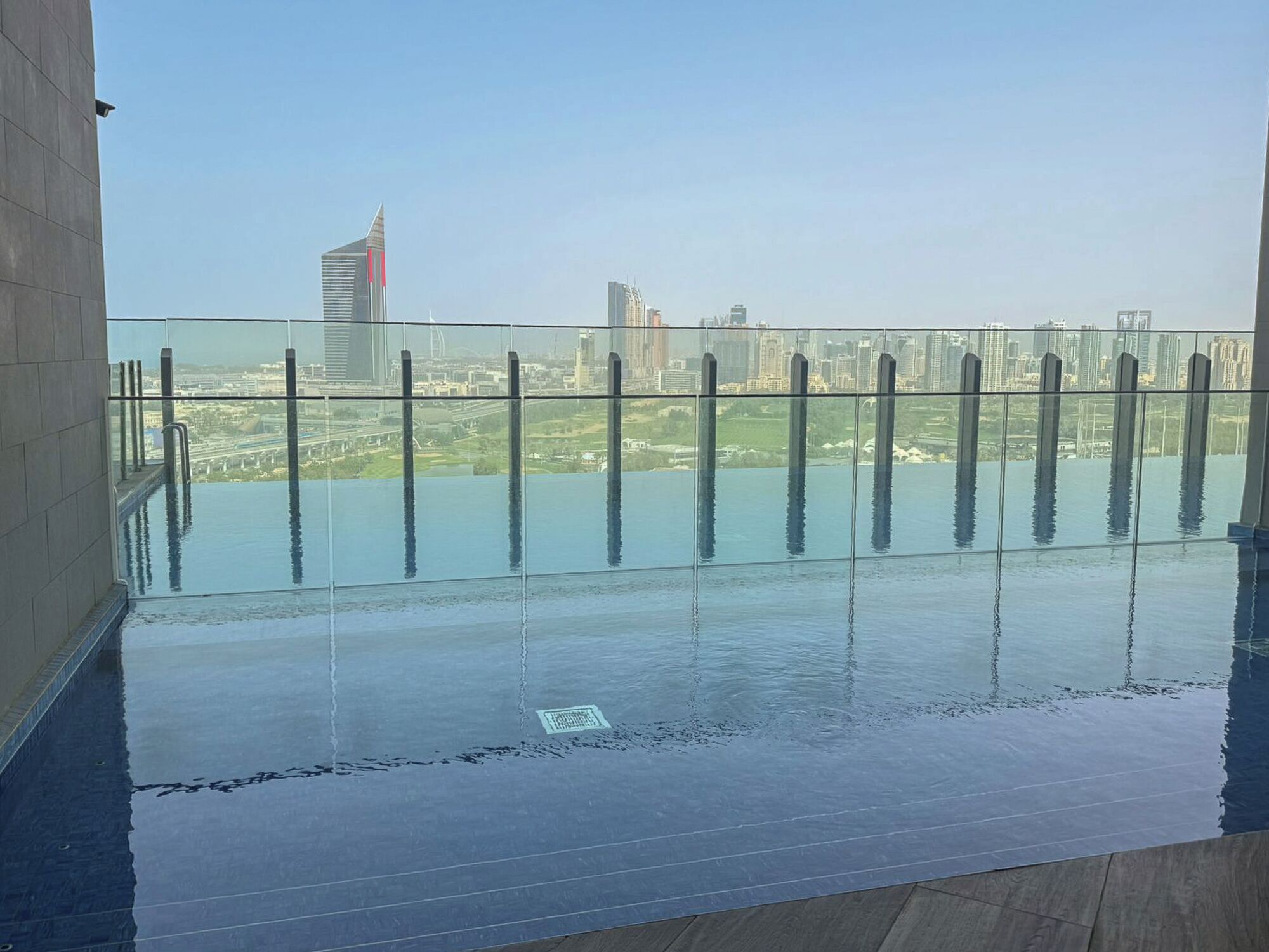 Una piscina infinita en la azotea con vistas a la ciudad, rodeada por una barandilla de vidrio.