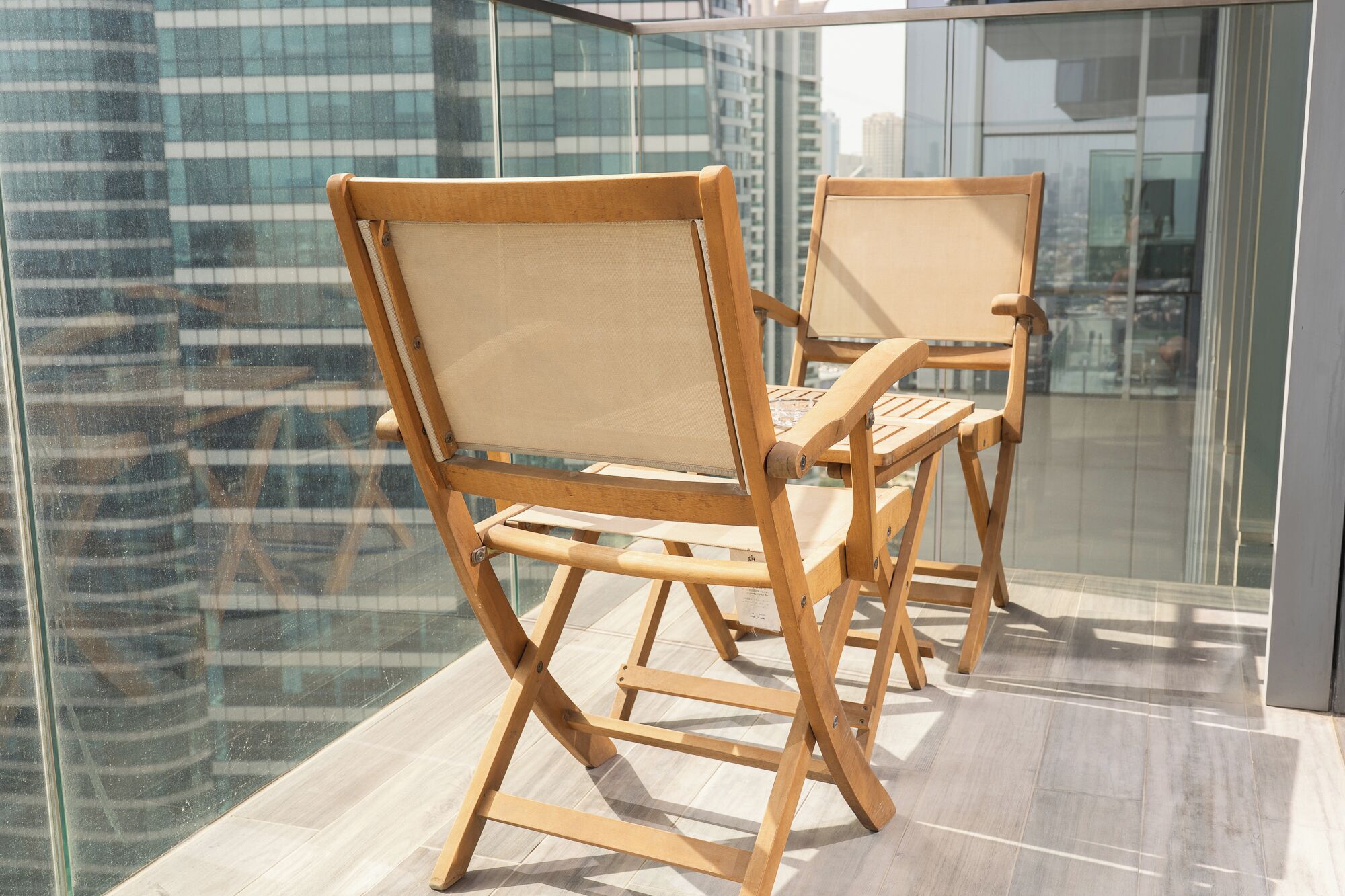 Two wooden chairs with mesh backs and metal legs, placed on a balcony with a glass railing.