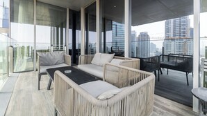 Ein moderner Balkon mit Korbmöbeln, Glasgeländern und Blick auf die Stadt.