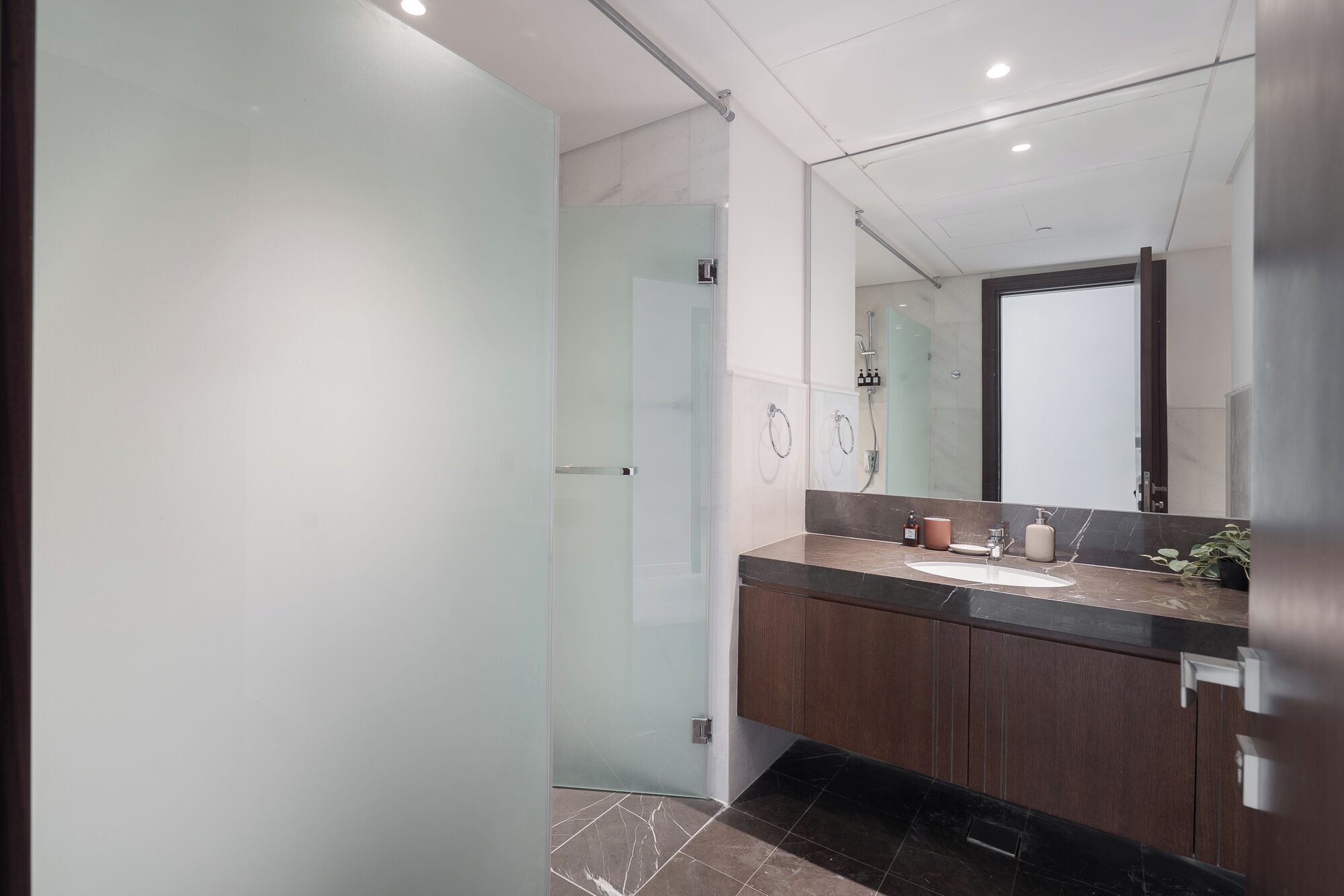 A modern bathroom with a glass shower enclosure, a large mirror, and dark wood cabinets.