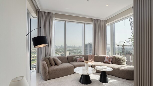 Ein modernes Wohnzimmer mit einer Eckcouch, zwei runden Tischen und großen Fenstern mit Blick auf die Stadt.