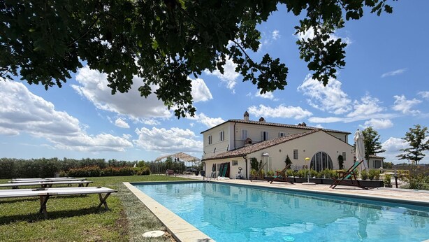 Ein Pool mit einer Terrassenanlage, ein großes Gebäude mit einem Ziegeldach und ein klarer Himmel.