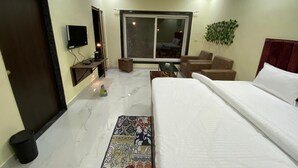 Une chambre d’hôtel équipée d’un lit, d’une télévision, d’un bureau, d’une chaise, d’un canapé, d’une fenêtre et d’un ventilateur de plafond.