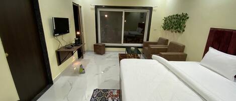 A hotel room with a bed, a TV, a desk, a chair, a sofa, a window, and a ceiling fan.