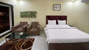 Une chambre d’hôtel comprenant un lit, deux fauteuils, une petite table, un mur végétal décoratif et un ventilateur de plafond.