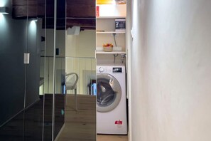 A laundry room with a washing machine, a shelf with a basket, and a chair. - Luxury apartament in SS annunziata (Firenze)