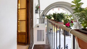 Un balcón con plantas en macetas, una puerta de madera y un equipo de aire acondicionado blanco.
