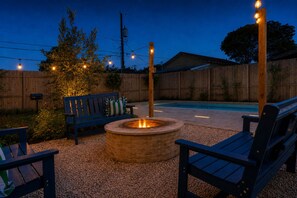 A backyard with a fire pit, wooden deck, and a pool. - NEW Paix Bleu Dragonfly Cottage  Private Pool &Spa | Pets (Galveston)