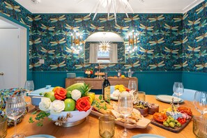 A dining table with a variety of food and drinks, a mirror, and teal wallpaper with a floral pattern. - NEW Paix Bleu Dragonfly Cottage  Private Pool &Spa | Pets (Galveston)