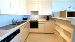 Una cocina compacta con armarios blancos, lavavajillas, cafetera y una pequeña encimera.