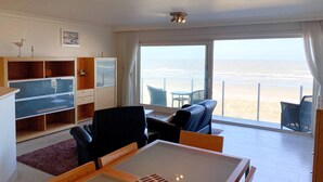 Una habitación con un ventanal grande con vistas a una playa, una mesa de comedor y una zona de estar con sillas.