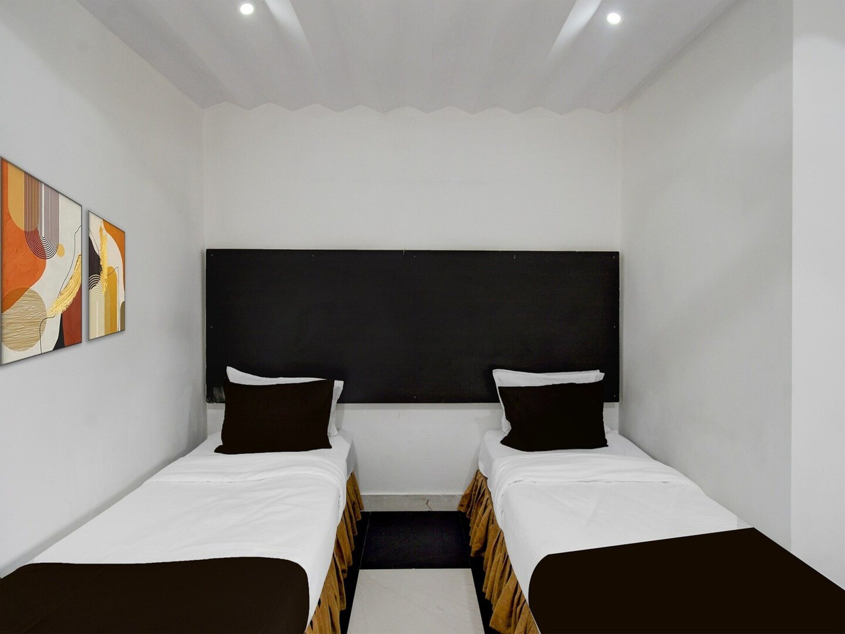 Ein kleines, modernes Zimmer mit zwei Einzelbetten, einem schwarzen Kopfteil und abstrakter Wandkunst.