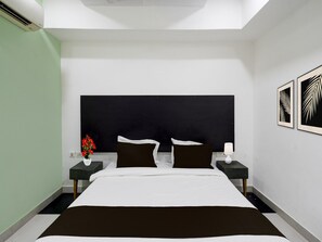 Ein modernes Hotelzimmer mit einem großen Bett, zwei Nachttischen, einem schwarzen Kopfteil und gerahmten Bildern an der Wand.