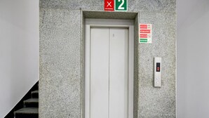 Een lift met een digitaal scherm, een rookvrij bord en noodinstructies op de muur.