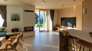 A modern living room with a fireplace, wooden furniture, a large TV, and a view of the outdoors.
