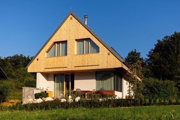 A two-story wooden house with a sloped roof, large windows, and a stone wall in the front. - Alpine Escape: 3BR Villa with Private Jacuzzi & Sauna in Bohinj (Bohinj)