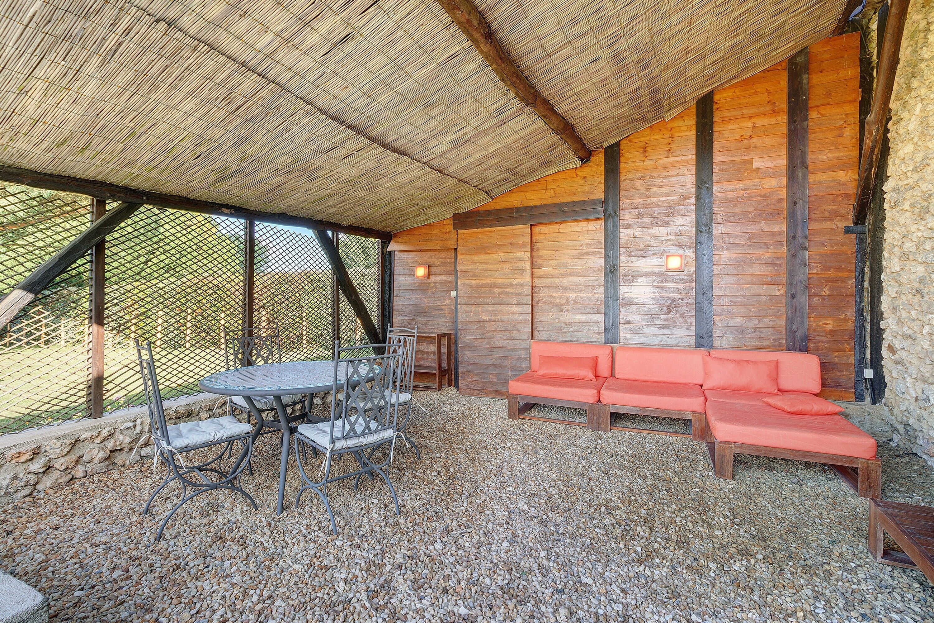 Un espace extérieur abrité, avec une table et des chaises, un canapé rouge et un mur en pierre.