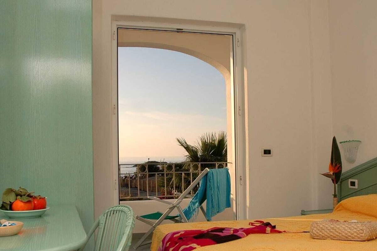 A room with a bed, a chair, a table, and a view of the outdoors.