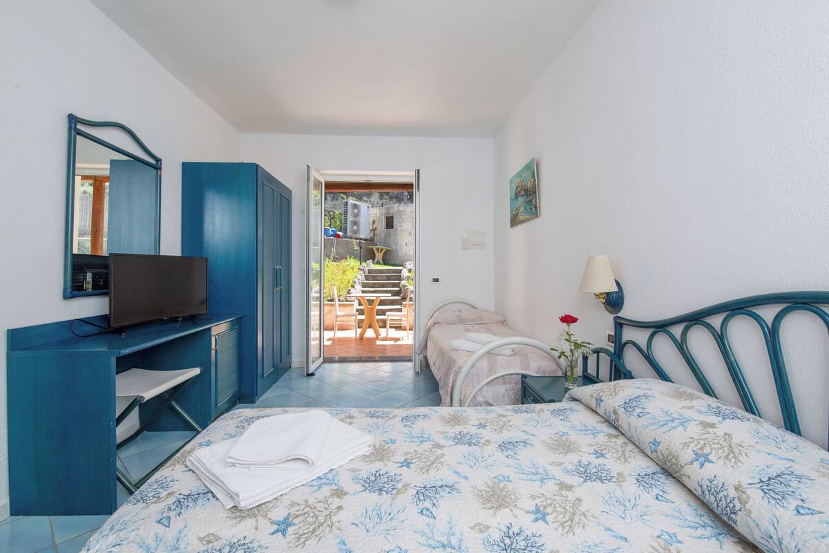 A bedroom with a bed, a TV, a desk, and a door leading to an outdoor area.