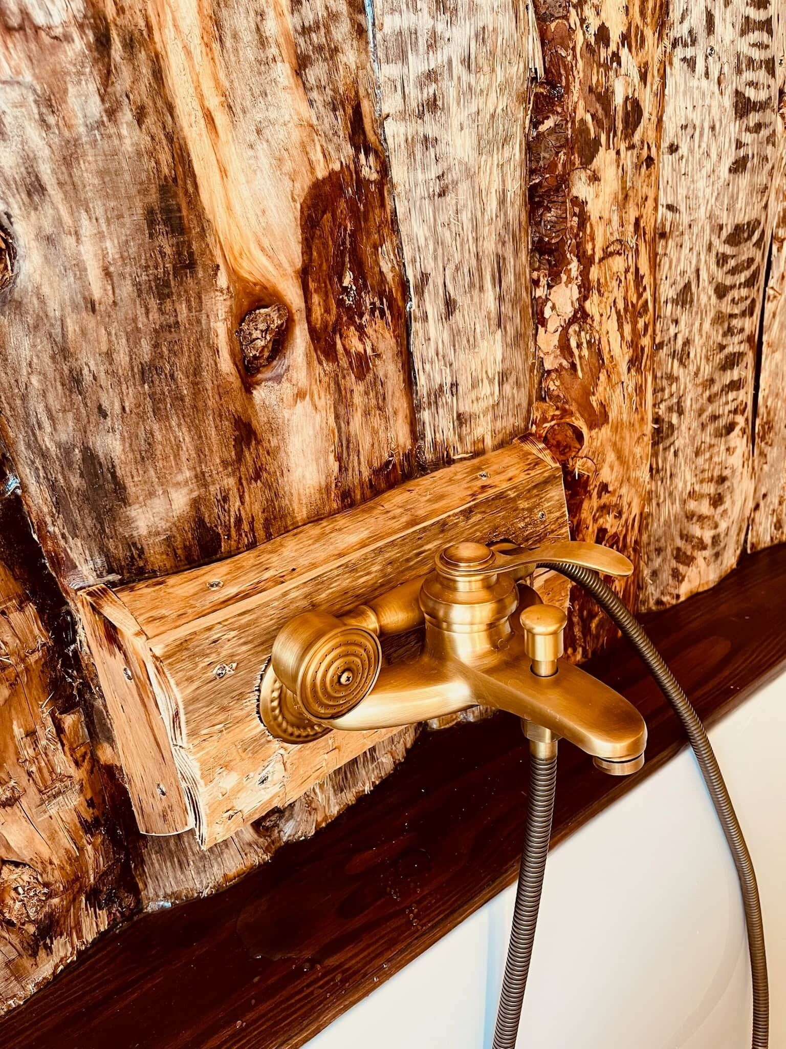 Une salle de bain avec un mur en bois, un robinet en laiton et une tuyauterie apparente.