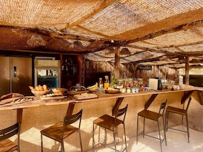 A rustic bar area with a wooden counter, chairs, and a variety of food and drink items. - Finca Lessya Estate, Cocon du Patio Lodge (Mauguio)