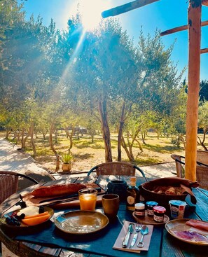 An outdoor dining area with a table set for breakfast, including bread, fruit, and beverages.