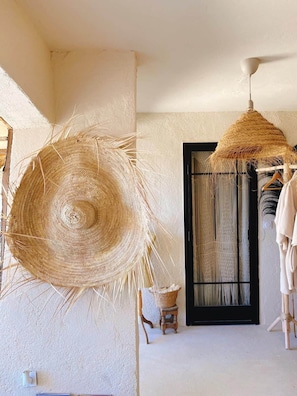 A room with a large woven basket, a hanging woven item, a black-framed window, and a small stool.