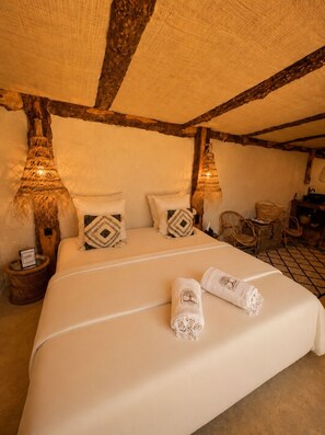 A cozy bedroom with a large bed, two nightstands with lamps, wicker furniture, and a tiled floor.