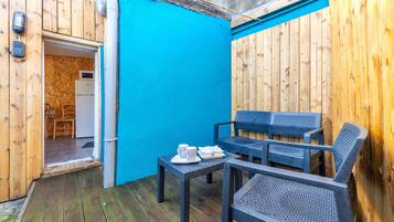 Una terraza de madera con un muro azul, un refrigerador blanco y una mesa con sillas.