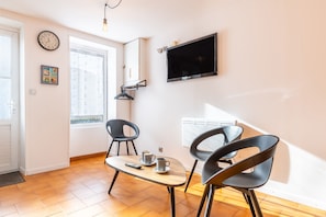 Una sala de estar moderna con televisor, dos sillones, una mesa, un reloj y un ventanal.