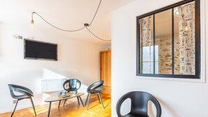 Une chambre moderne dotée d’une télévision, d’un plancher en bois et d’une grande fenêtre avec des rideaux.