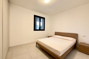 Ein Schlafzimmer mit einem hölzernen Bett, einem Nachttisch, einem kleinen Fenster und einer Leuchte.