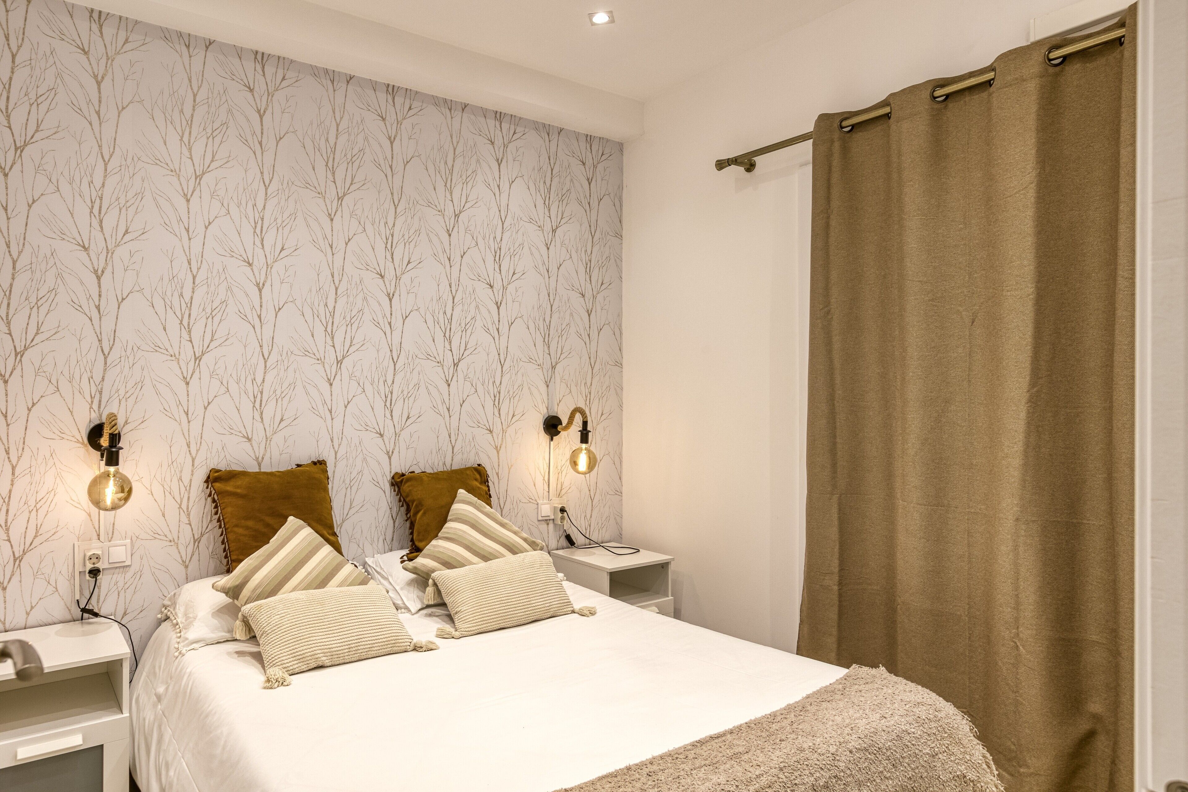 Een slaapkamer met een bed, twee nachtkastjes, een wandlamp en een gordijn.