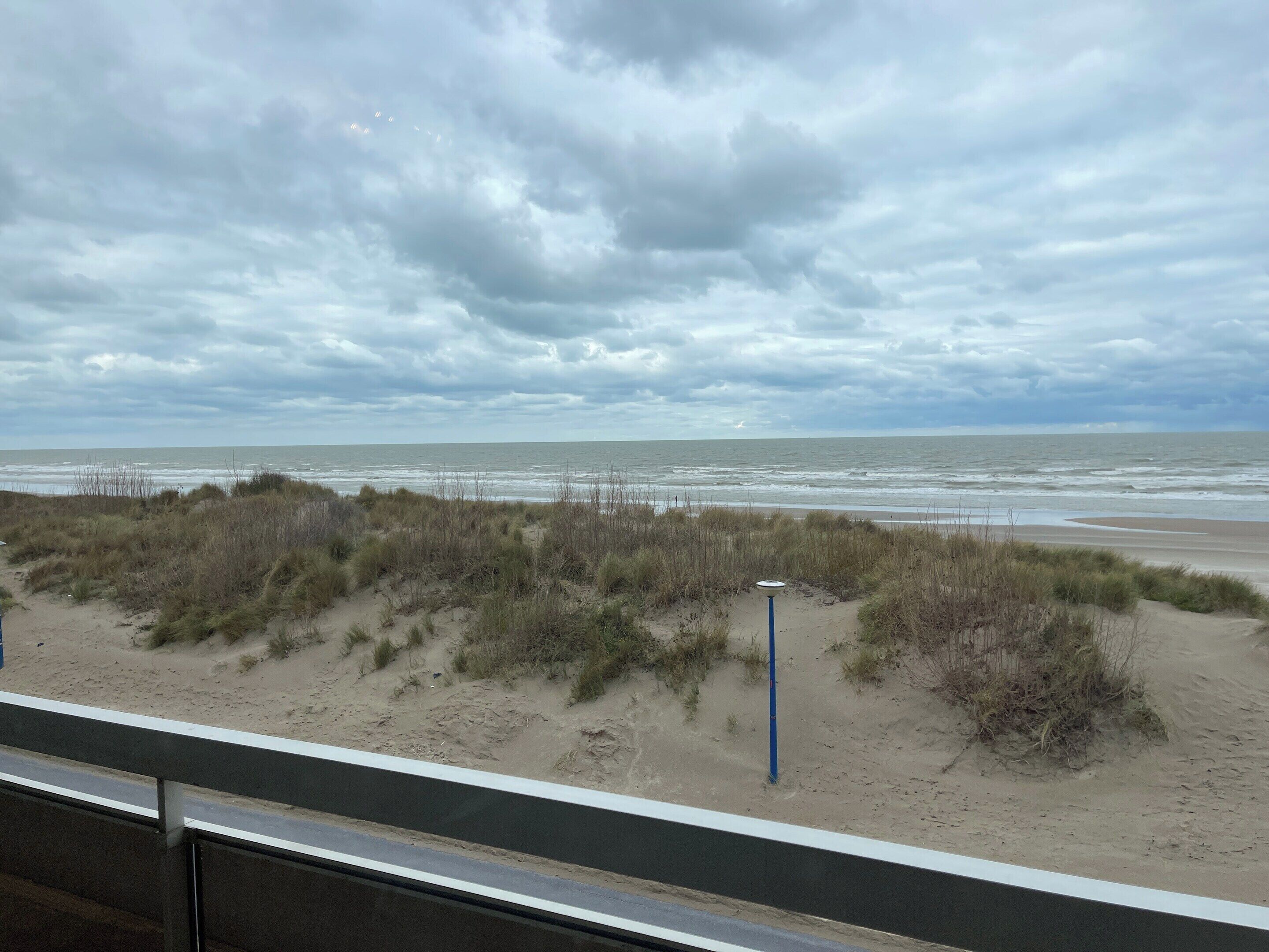 A beach view with dunes and a cloudy sky.