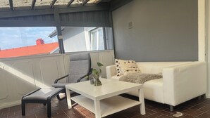 Un balcon avec une table blanche, une chaise grise et un canapé blanc.