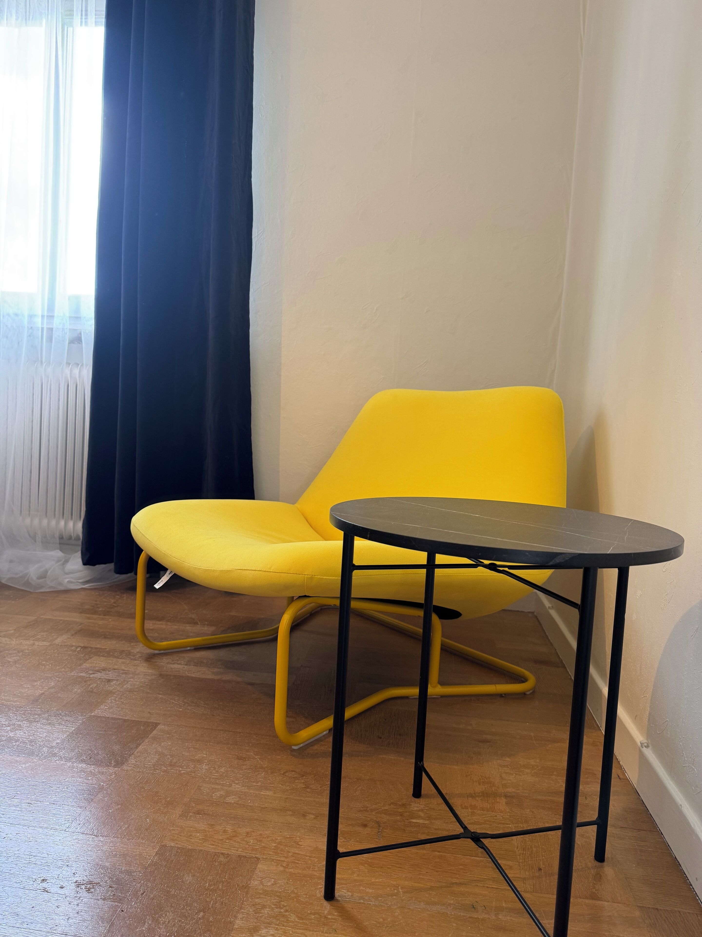 A yellow chair and a small black table in a room with wooden flooring and a white wall.