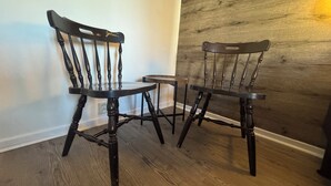 Deux chaises en bois foncé, dotées d’un dossier incurvé et de pieds tournés, sont placées sur un plancher en bois, adossées à un mur blanc et à un mur recouvert de panneaux en bois.