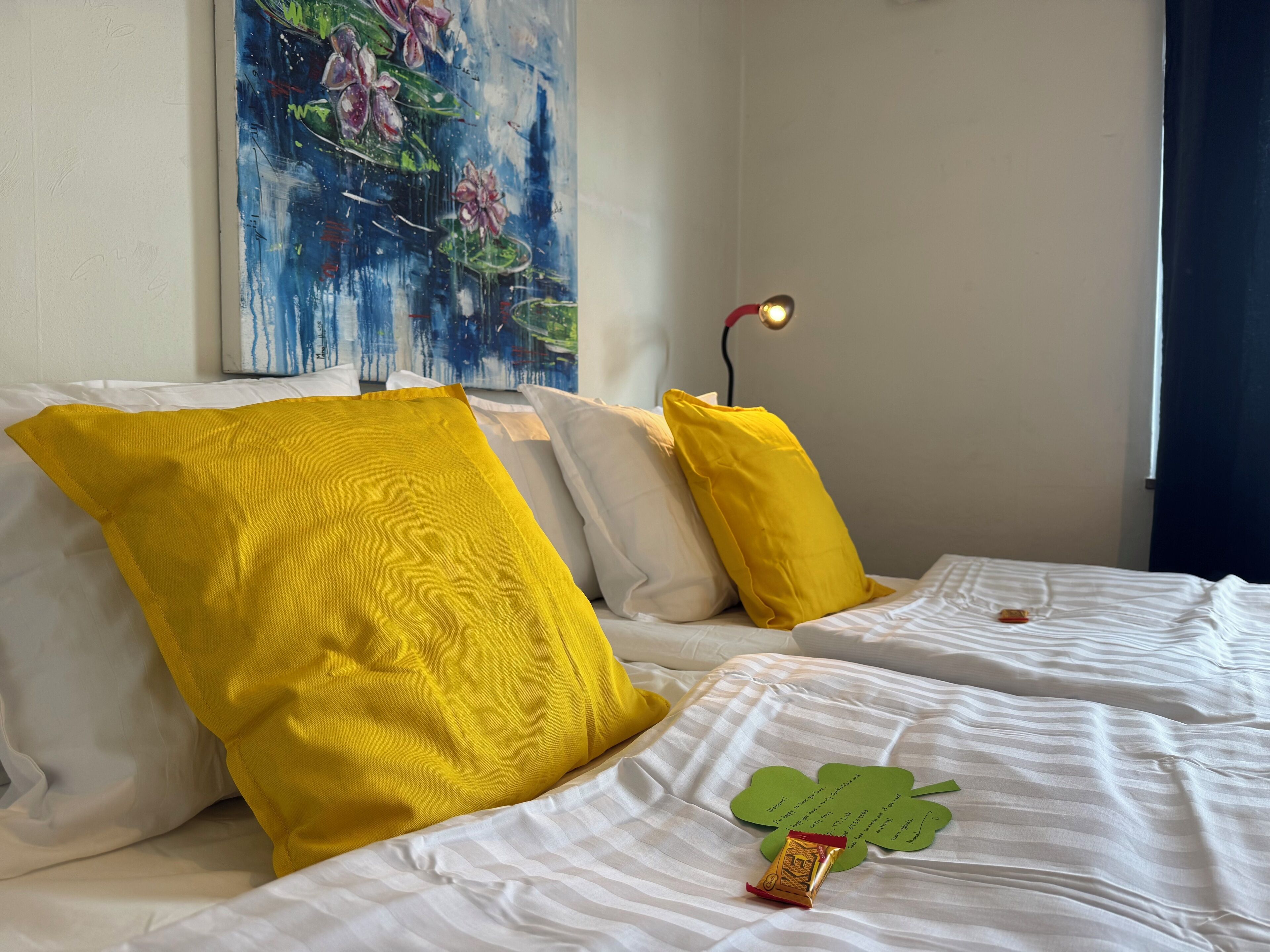 A hotel room with a bed featuring white bedding and two large yellow pillows. A green shamrock-shaped object is placed on the bed.