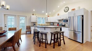 A modern kitchen with white cabinets, a stainless steel refrigerator, and a central island with stools. - Ski-In Hot Tub | Sunburst Drive Mountain Home (Sun Peaks)