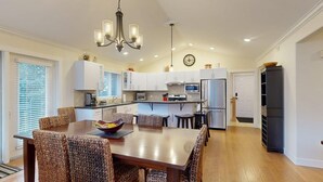 A modern kitchen with white cabinets, a dining area with wicker chairs, and a chandelier. - Ski-In Hot Tub | Sunburst Drive Mountain Home (Sun Peaks)