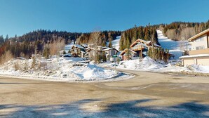 A ski resort with wooden cabins, a parking area, and a snowy mountain backdrop. - Ski-In Hot Tub | Sunburst Drive Mountain Home (Sun Peaks)