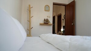 A bedroom with a bed, a coat rack, a shelf with a ship model, and a door leading to another room. - titryte (Aourir)