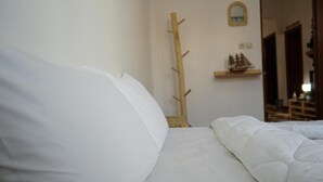 A neatly made bed with white bedding in a room with a wooden coat rack and a small shelf with a ship model. - titryte (Aourir)