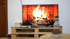 A television displaying a fireplace scene, placed on a wooden TV stand with books and a decorative item. - titryte (Aourir)